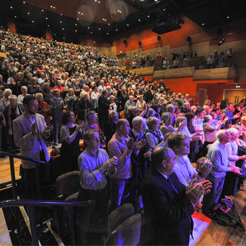 An audience standing and applauding a performance